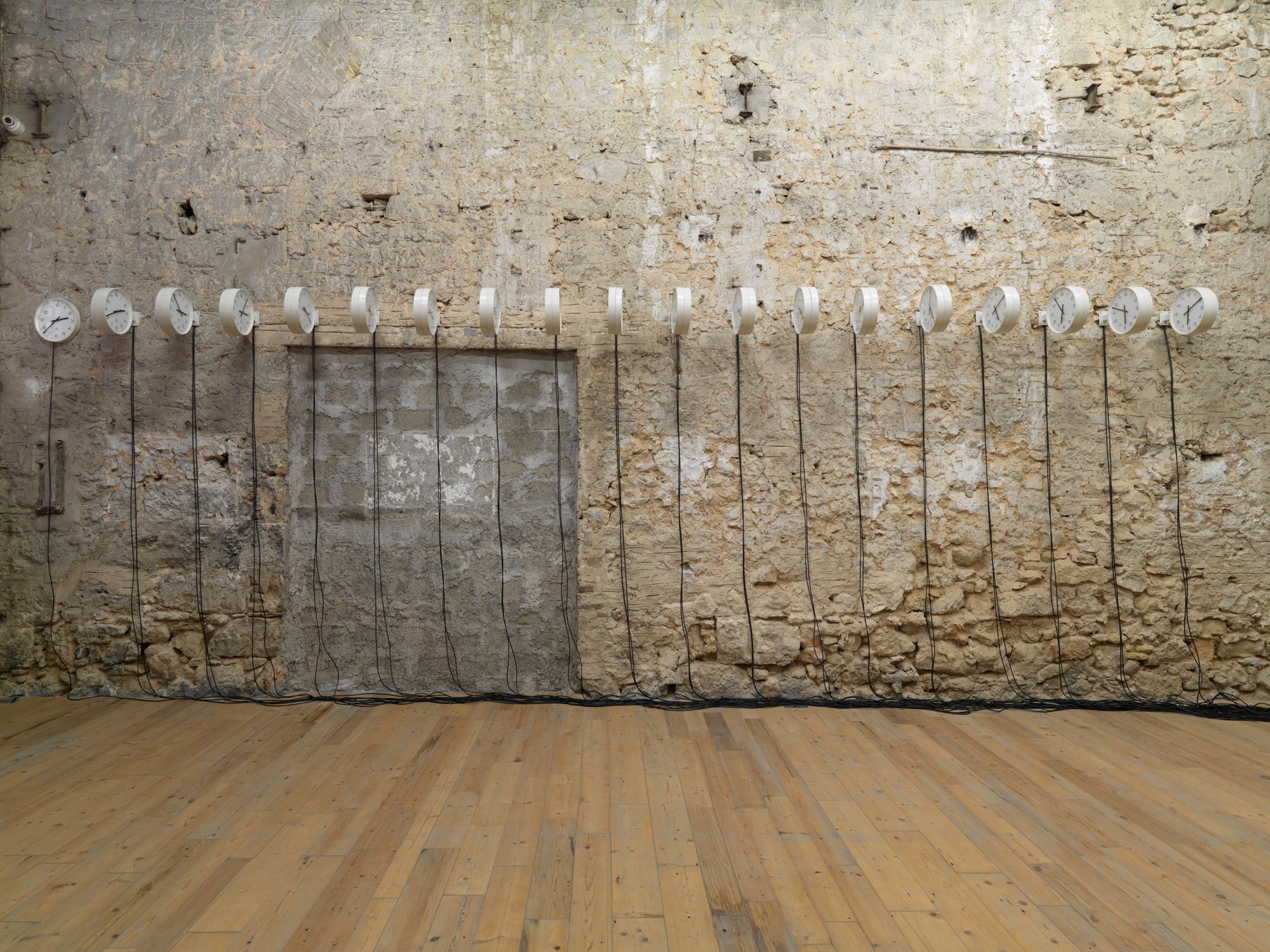 Iris Touliatou, mother arrangement, 37 clocks arranged in a row on one wall &amp; 3 mother clocks contained in server cabinet. Temporary Loan from the National Museum of Contemporary Art, Athens (EMST), Non-variable dimensions: 264 cm x 895 cm with 47 cm spacing between the clocks and 827 cm between the last clock and the cabinet, 2022.Installation view, Iris Touliatou, μητέρες, Rodeo, Piraeus, 2022.